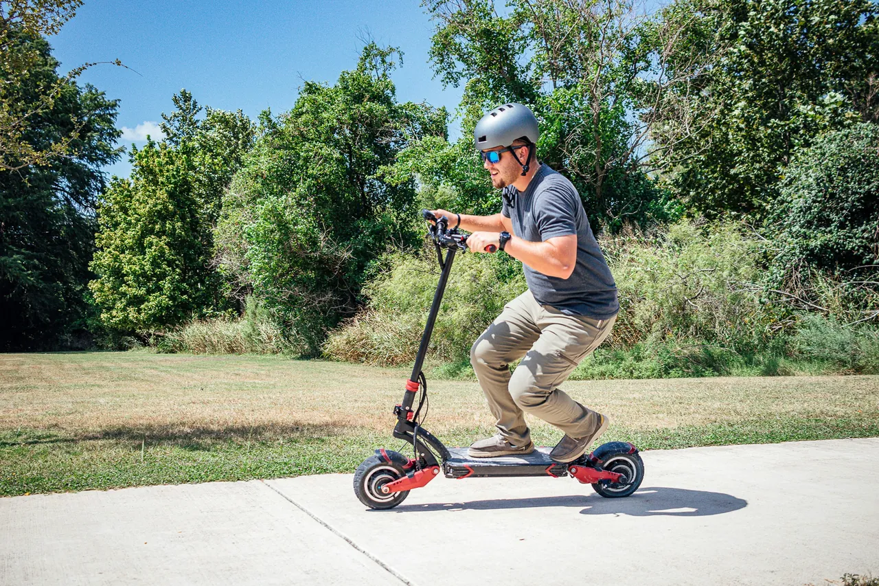 Helmeted rider on a black and red electric scooter on a paved path.