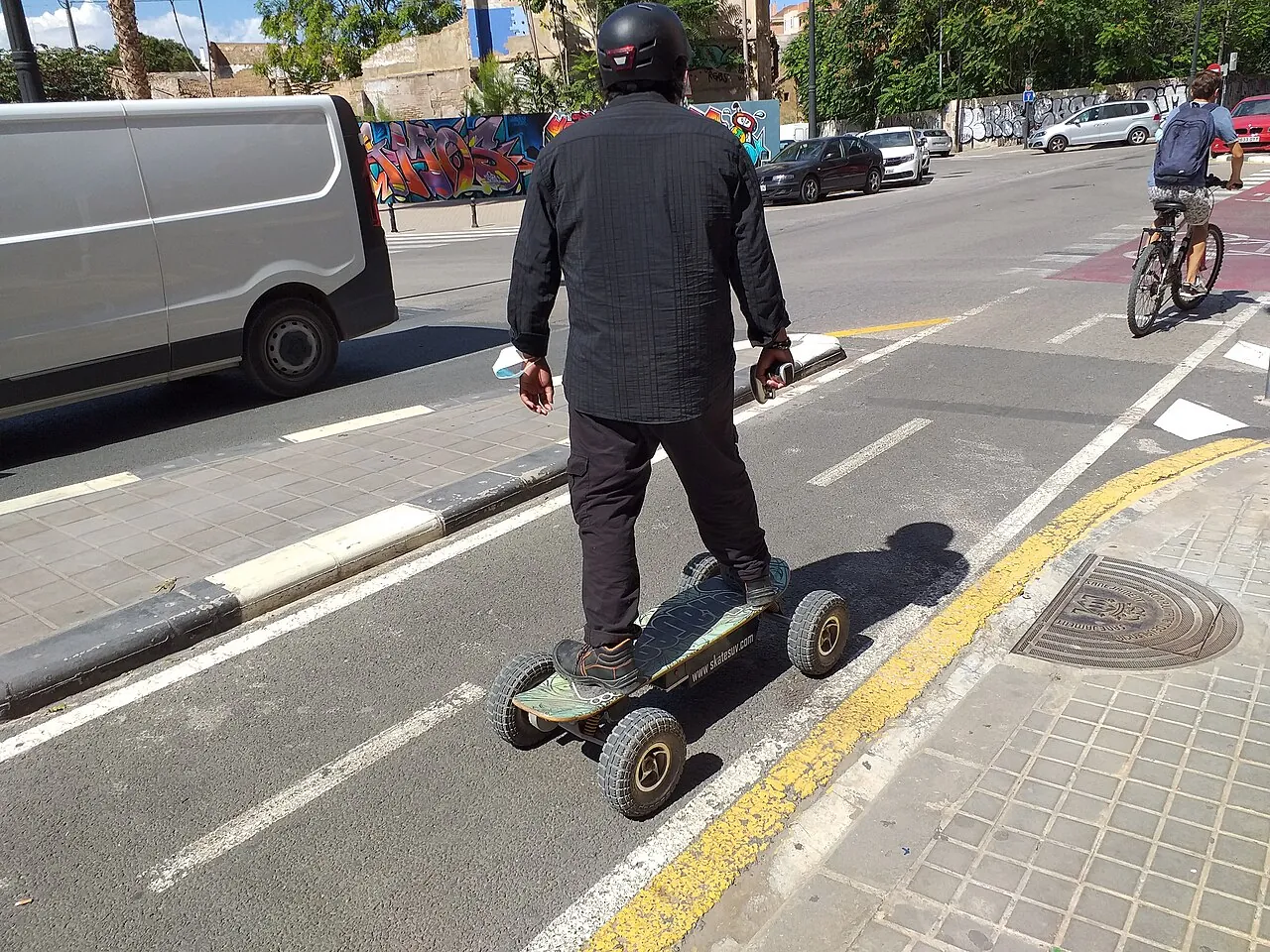 A helmeted rider on a pneumatic-tire electric skateboard in a separated bike lane.
