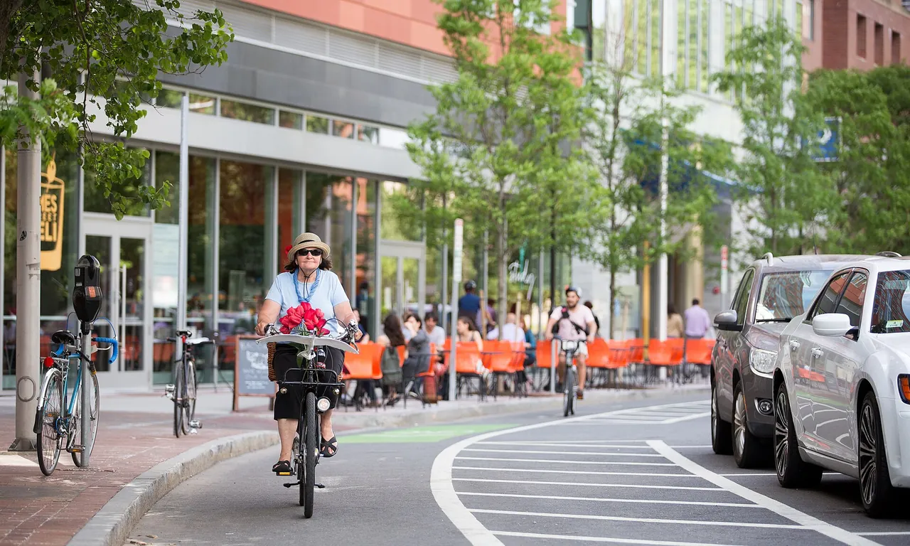 A helmeted cyclist carrying flowers rides along a parking-protected bike lane in Cambridge, Massachusetts.