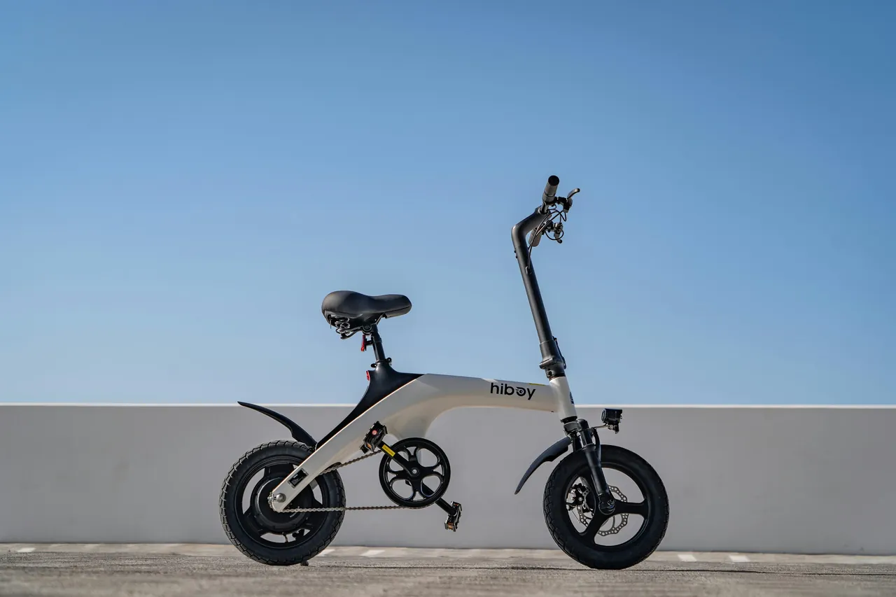 Compact white Hiboy electric bike against a pale wall and blue sky.