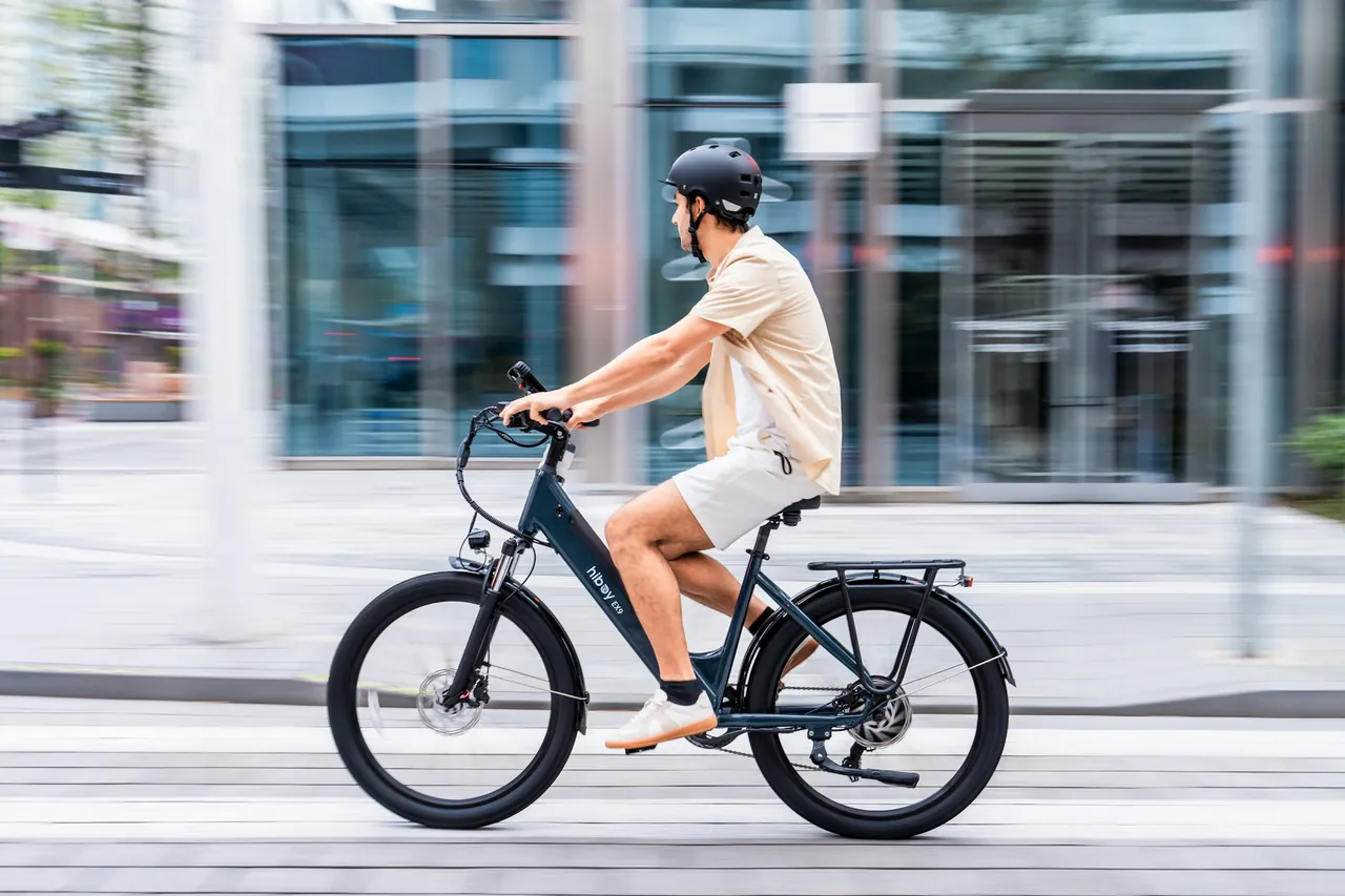 Helmeted rider on a dark step-through e-bike beside city buildings