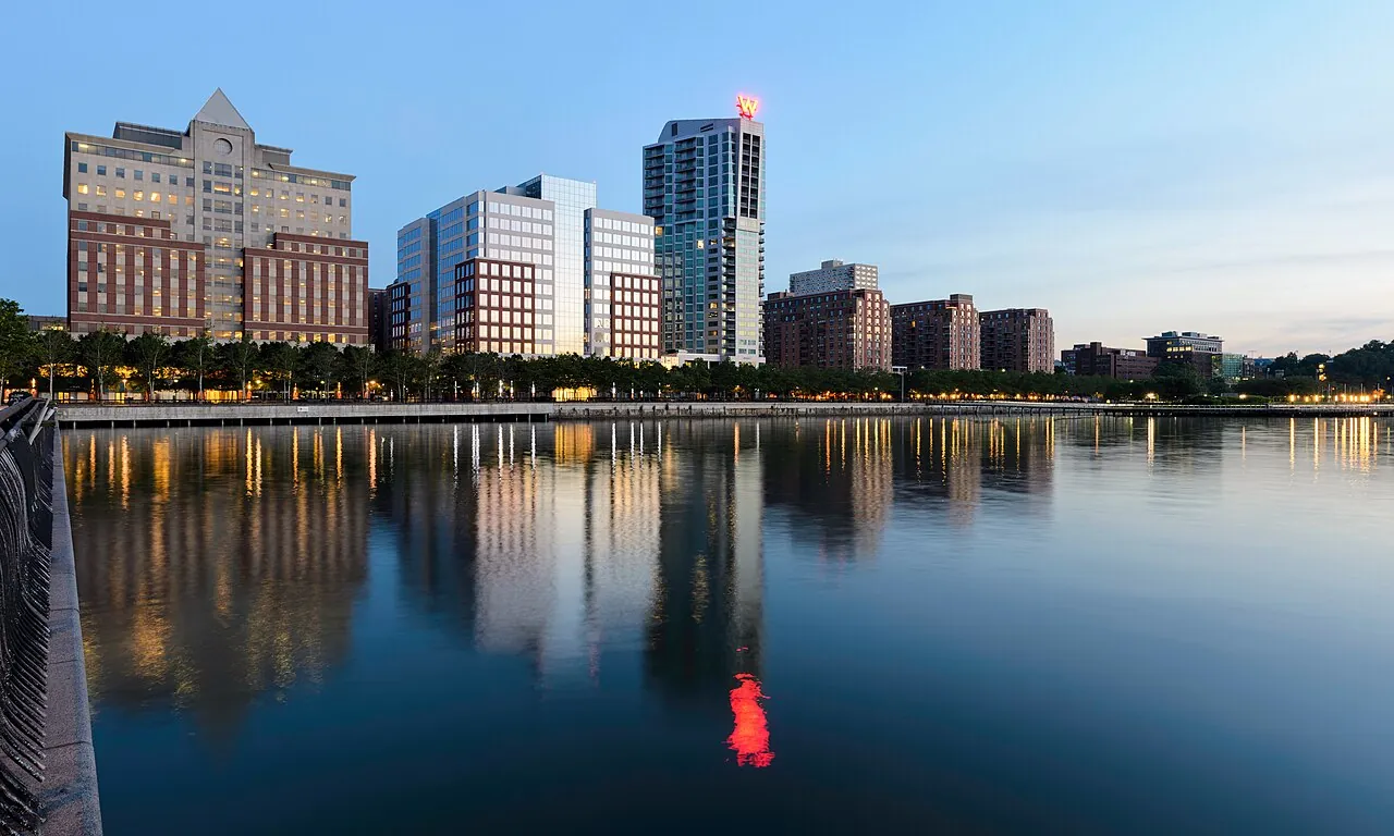 Hoboken's waterfront buildings reflected in still water at dusk.