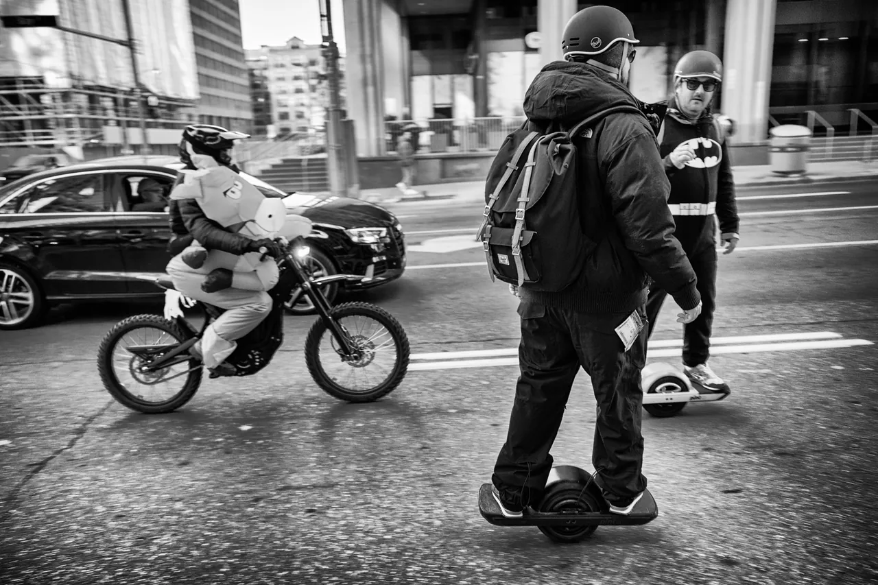 Helmeted Onewheel riders on a city street during a Halloween group ride.